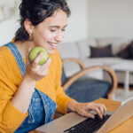 Meisje werkt op computer en eet een appel