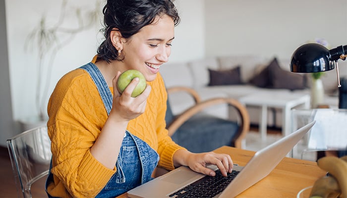 Meisje werkt op computer en eet een appel