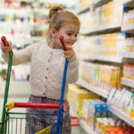 Meisje met klein boodschappenwagentje in supermarkt
