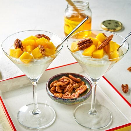 Twee glazen Griekse yoghurt met mango en pecannoten