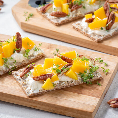 Twee volkoren crackers met roomkaas, mango en pecannoten