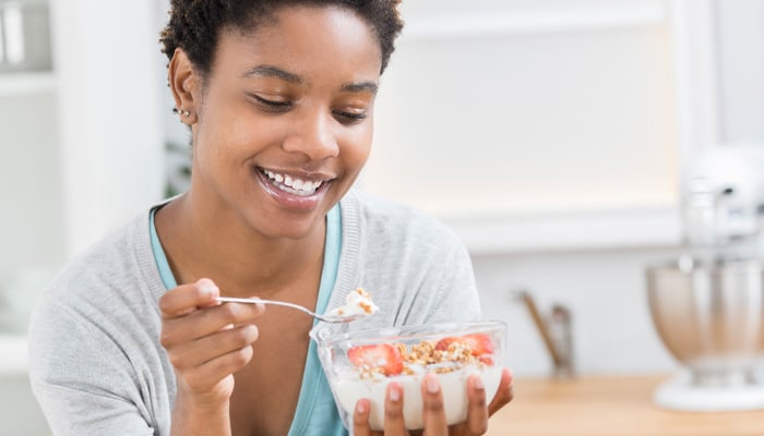 Vrouw eet kommetje yoghurt met granola en fruit