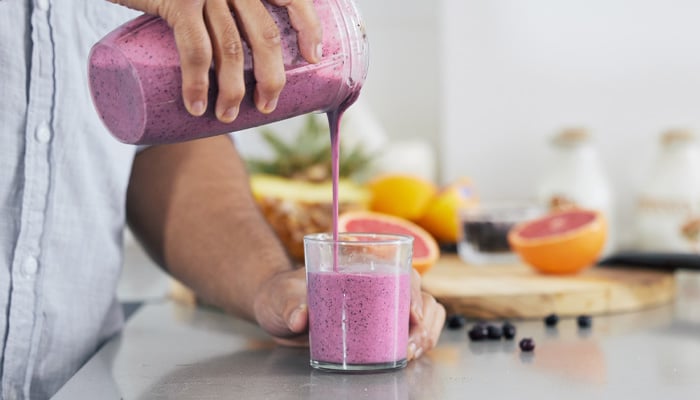 Iemand schenkt een smoothie in vanuit een blender