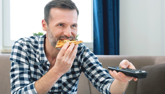 Man eet pizza en zapt met een afstandsbediening
