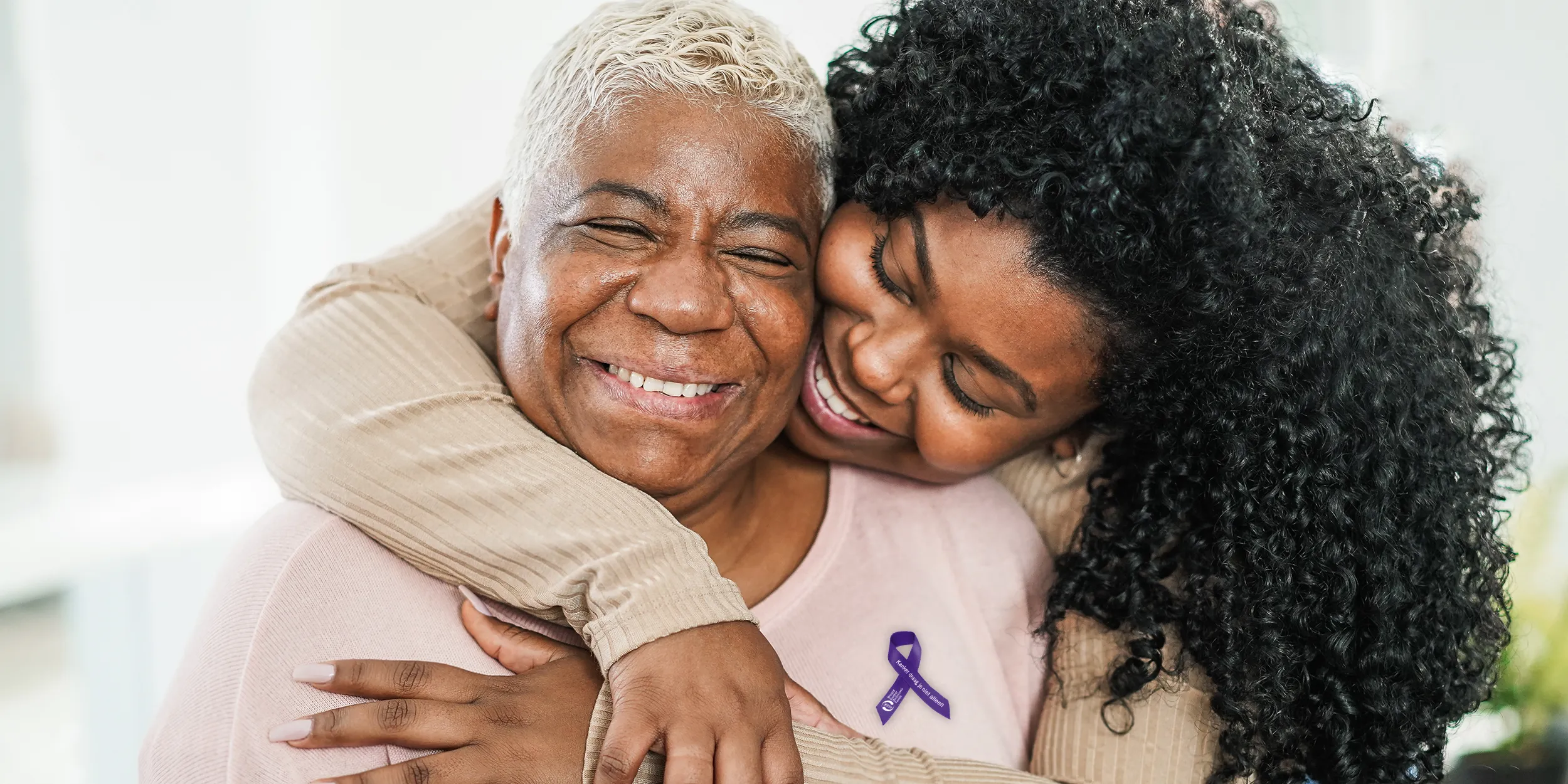 Dochter omhelst moeder. Op de trui van de moeder is het paarse lintje opgespeld.
